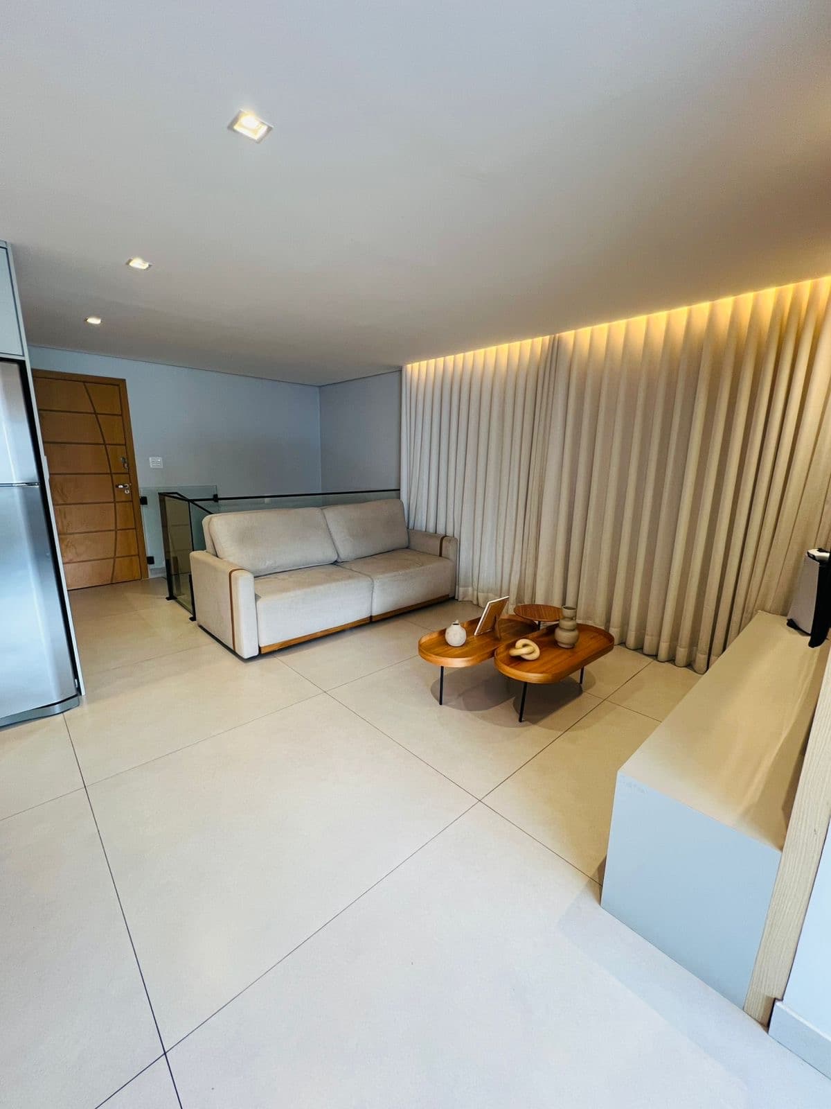 Sala de estar com sofá branco, cortinas e iluminação indireta em LED