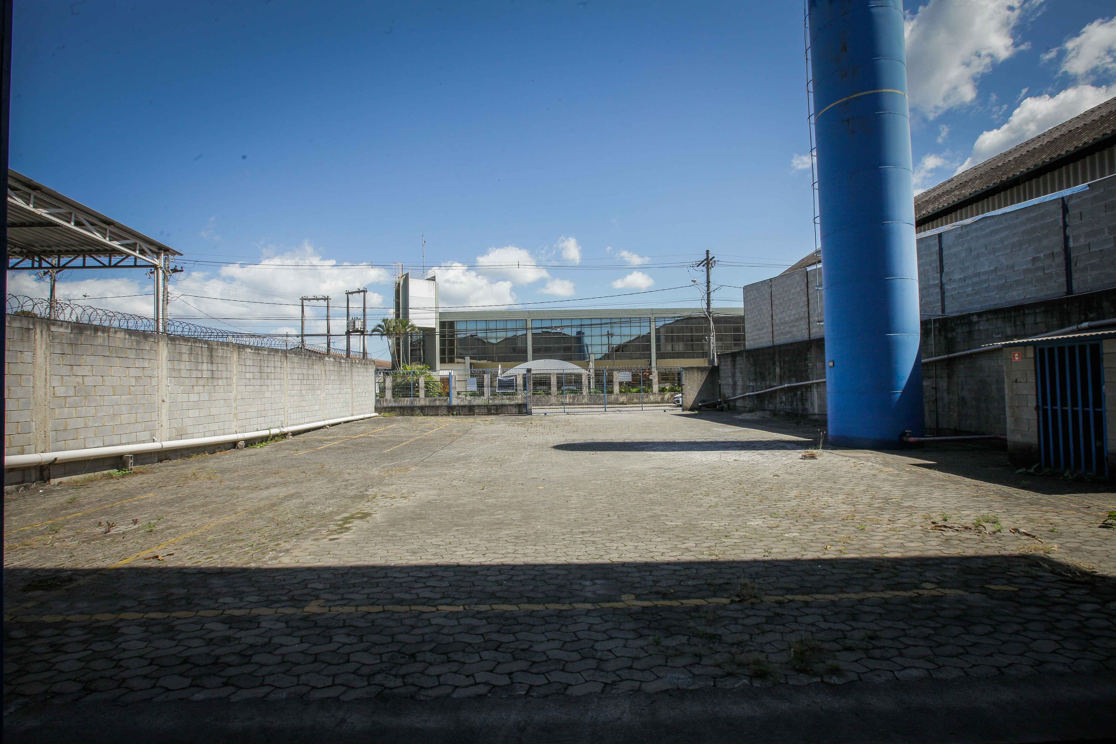 Pátio de manobra pavimentado, cercado por muro, com portão ao fundo